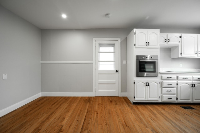 kitchen with white cabinets, oven, and light wood-type flooring