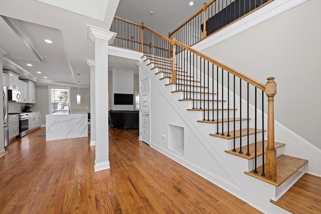 stairs featuring wood-type flooring, ornate columns, and crown molding