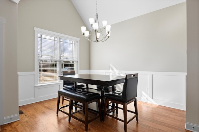 dining space with light wood-type flooring, lofted ceiling, and an inviting chandelier