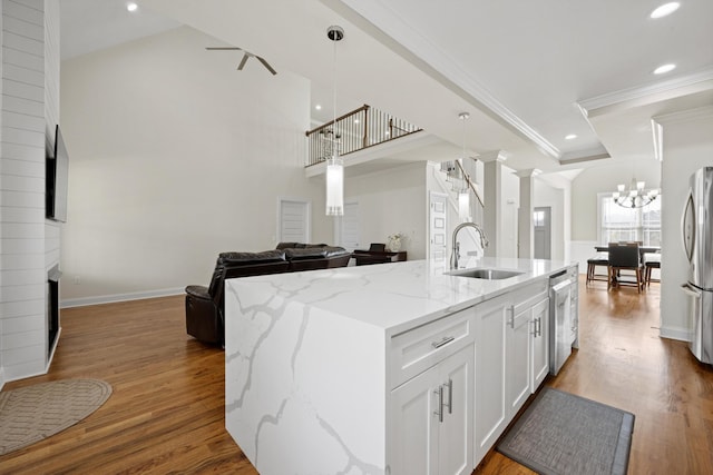 kitchen with decorative light fixtures, sink, white cabinetry, and an island with sink