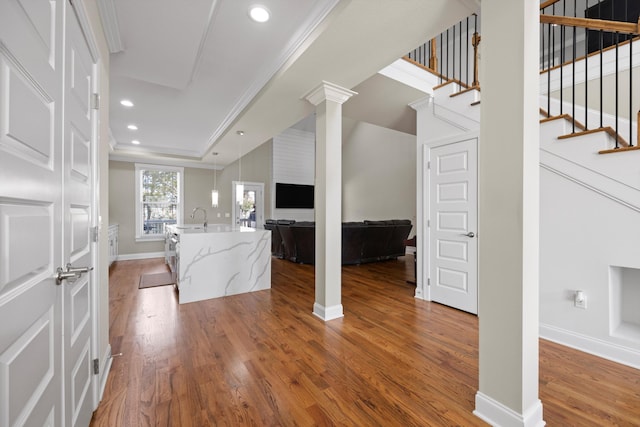 unfurnished living room with a tray ceiling, crown molding, sink, and wood-type flooring