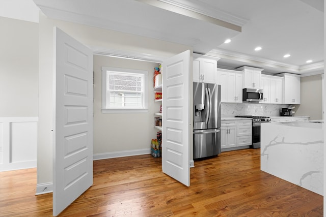 kitchen featuring light stone countertops, stainless steel appliances, light hardwood / wood-style floors, white cabinets, and ornamental molding