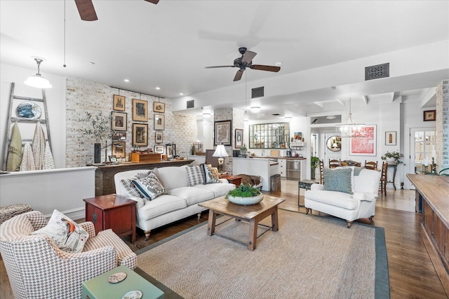 living room featuring ceiling fan with notable chandelier, wood-type flooring, and brick wall