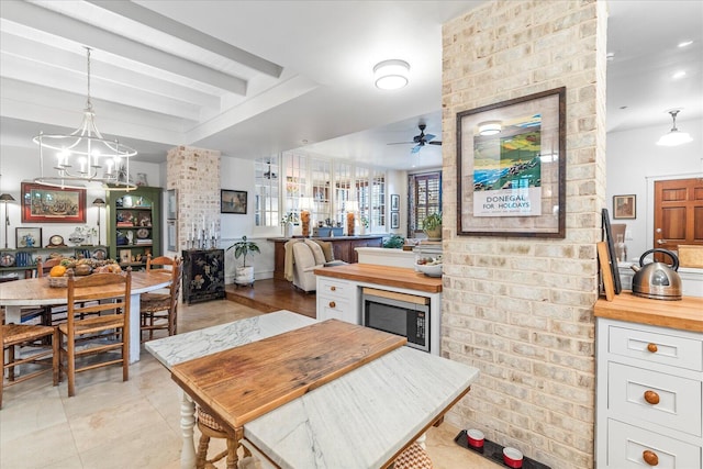 kitchen featuring butcher block countertops, built in microwave, hanging light fixtures, ceiling fan with notable chandelier, and white cabinets