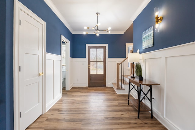 foyer entrance featuring light wood-type flooring, ornamental molding, and an inviting chandelier