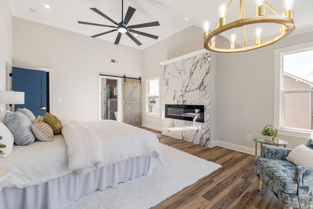 bedroom featuring dark hardwood / wood-style flooring, ceiling fan with notable chandelier, crown molding, a barn door, and a premium fireplace