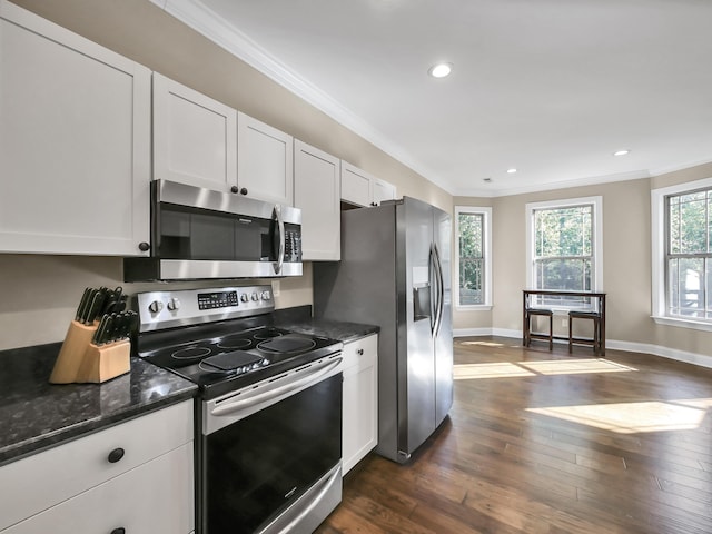 kitchen with dark stone countertops, white cabinetry, stainless steel appliances, and ornamental molding