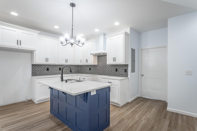 kitchen featuring premium range hood, white cabinets, sink, pendant lighting, and an island with sink