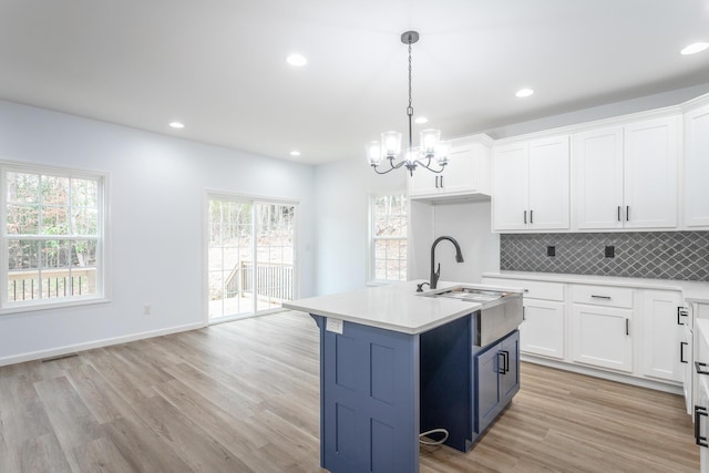 kitchen with decorative light fixtures, decorative backsplash, sink, a kitchen island with sink, and light hardwood / wood-style flooring