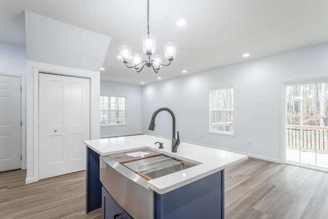 kitchen with light hardwood / wood-style flooring, hanging light fixtures, blue cabinets, a kitchen island with sink, and a chandelier