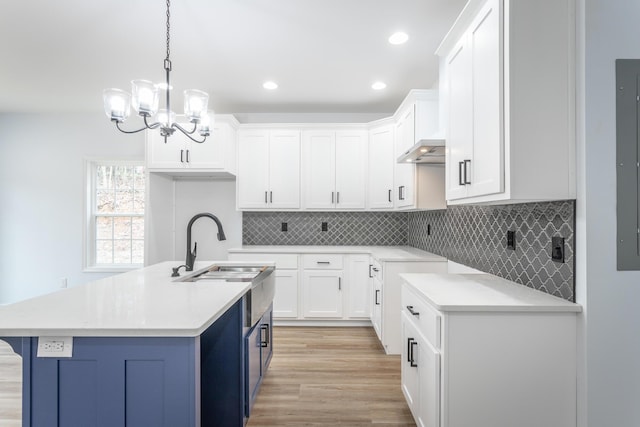 kitchen with decorative light fixtures, sink, white cabinetry, a notable chandelier, and a center island with sink