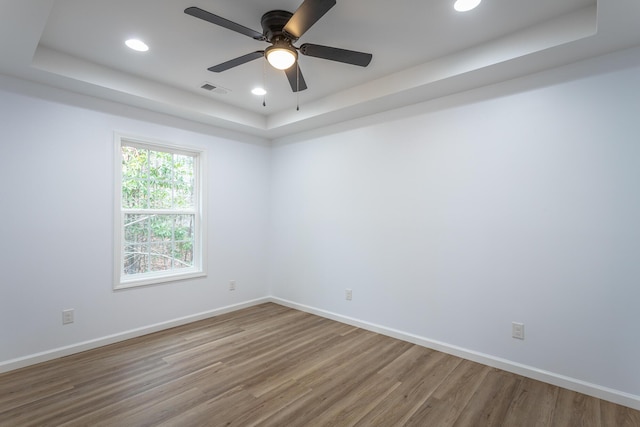 empty room featuring hardwood / wood-style flooring, ceiling fan, and a raised ceiling