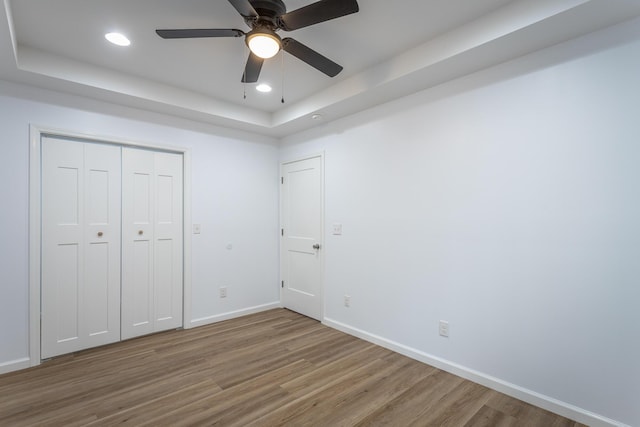 unfurnished bedroom with hardwood / wood-style floors, a closet, a tray ceiling, and ceiling fan