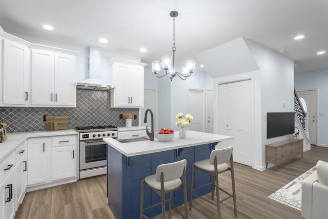 kitchen featuring wall chimney range hood, an island with sink, white cabinets, and stainless steel stove