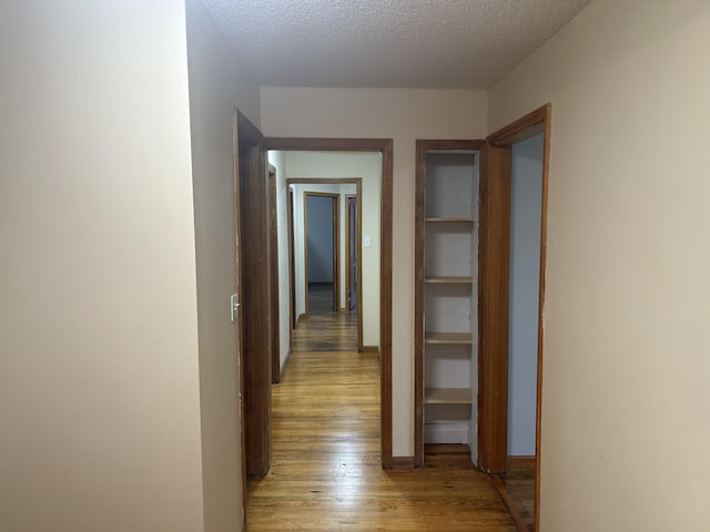 corridor with baseboards, light wood-style flooring, and a textured ceiling