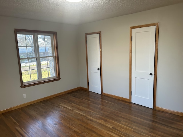 unfurnished bedroom featuring a textured ceiling, dark wood-style flooring, and baseboards