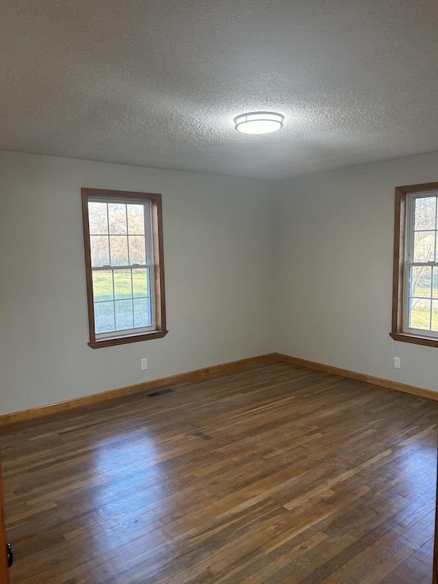 spare room featuring a textured ceiling, dark wood-type flooring, visible vents, and baseboards