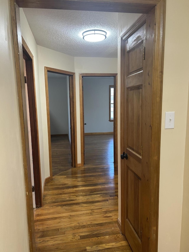 hallway with baseboards, dark wood-type flooring, and a textured ceiling