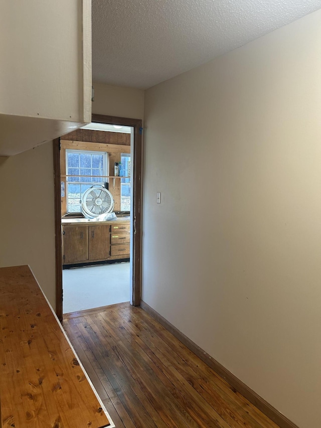 hallway with dark wood-style floors, a textured ceiling, and baseboards