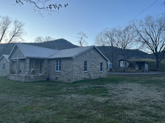 view of side of home with metal roof, brick siding, a yard, crawl space, and a storage unit