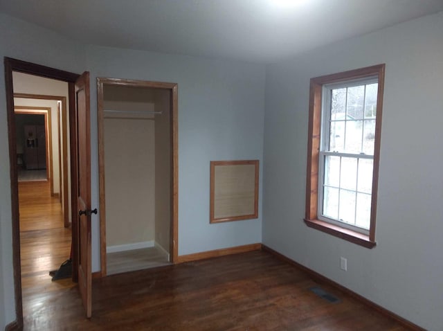 unfurnished bedroom with dark wood-type flooring, multiple windows, visible vents, and baseboards