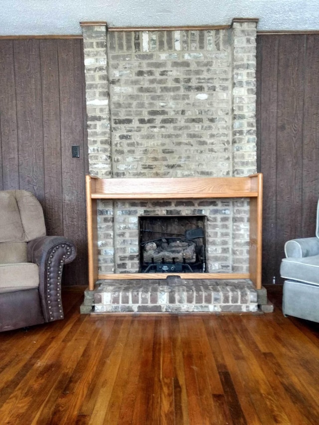 living area with a fireplace, wooden walls, a textured ceiling, and wood finished floors