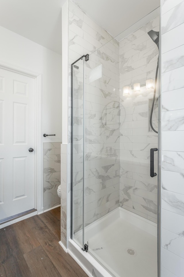 bathroom featuring hardwood / wood-style floors, a shower with door, toilet, and tile walls