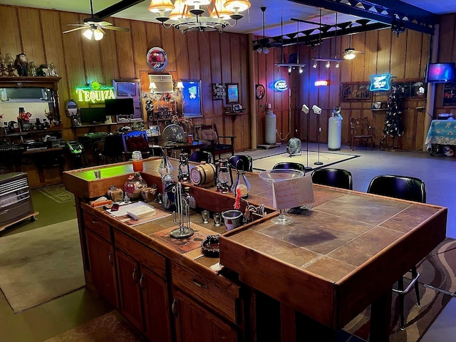 interior space featuring carpet flooring, ceiling fan with notable chandelier, wood walls, and pendant lighting