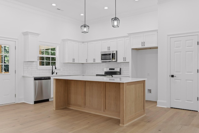 kitchen with white cabinets, a kitchen island, hanging light fixtures, and appliances with stainless steel finishes