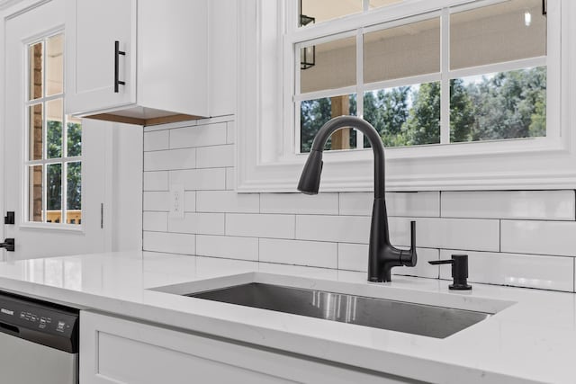 kitchen featuring light stone countertops, decorative backsplash, stainless steel dishwasher, sink, and white cabinetry