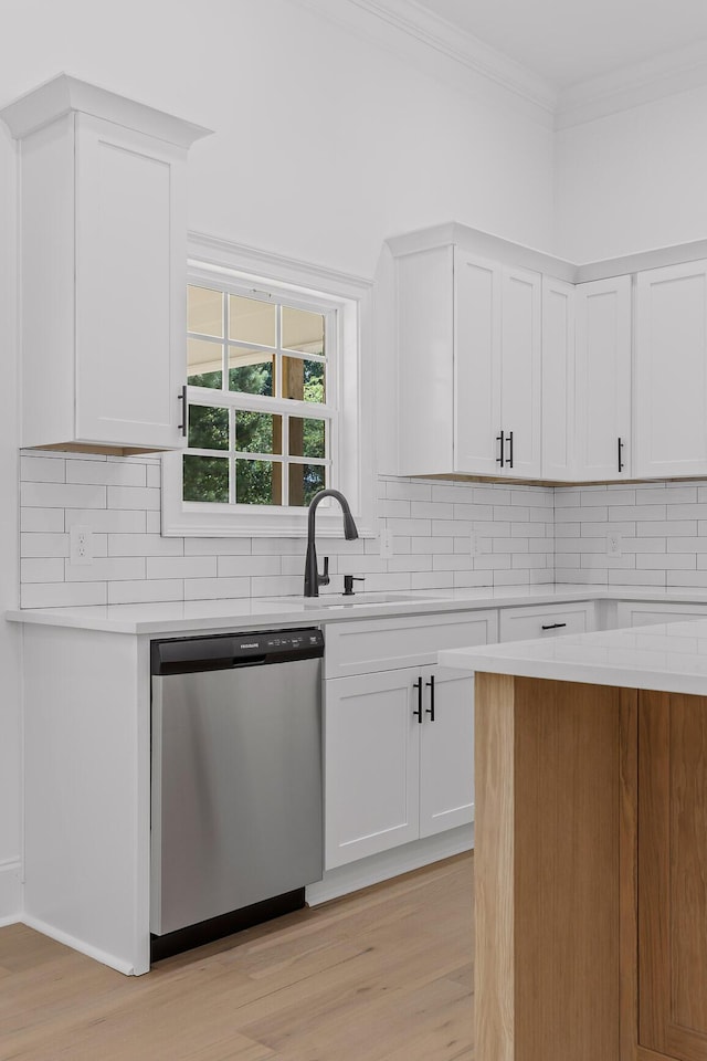 kitchen with white cabinetry, dishwasher, light hardwood / wood-style flooring, crown molding, and decorative backsplash