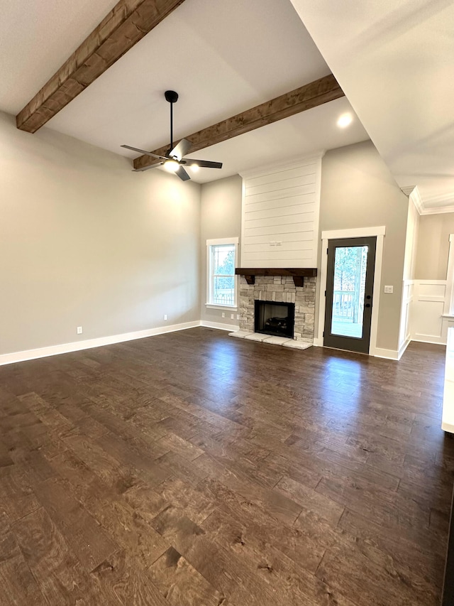 unfurnished living room featuring beam ceiling, a stone fireplace, a wealth of natural light, and ceiling fan