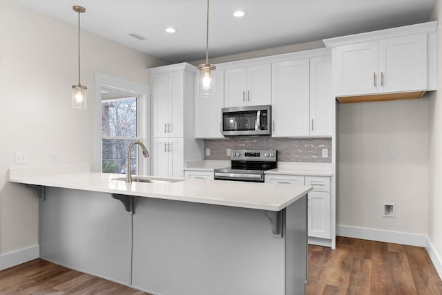 kitchen featuring hanging light fixtures, sink, appliances with stainless steel finishes, a kitchen bar, and white cabinetry