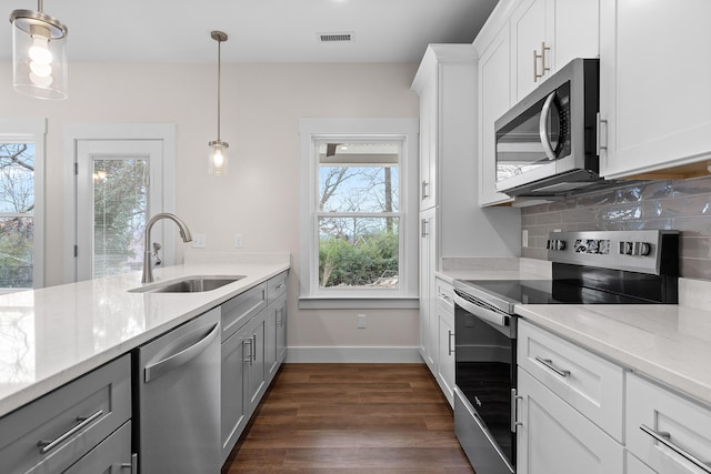 kitchen with light stone countertops, stainless steel appliances, sink, white cabinets, and hanging light fixtures