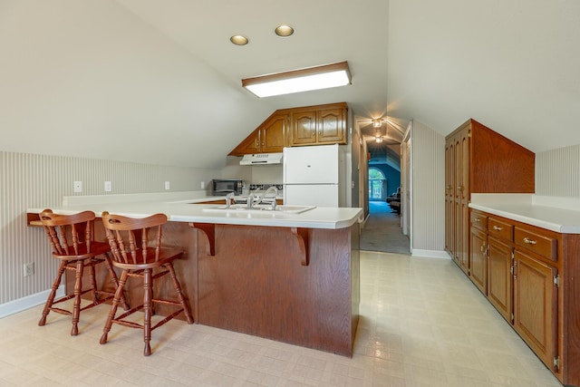 kitchen featuring a kitchen bar, sink, vaulted ceiling, and white refrigerator