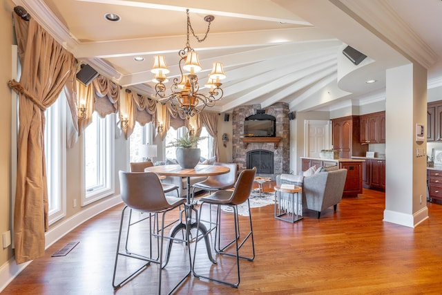 dining room featuring hardwood / wood-style floors, an inviting chandelier, a stone fireplace, and ornamental molding