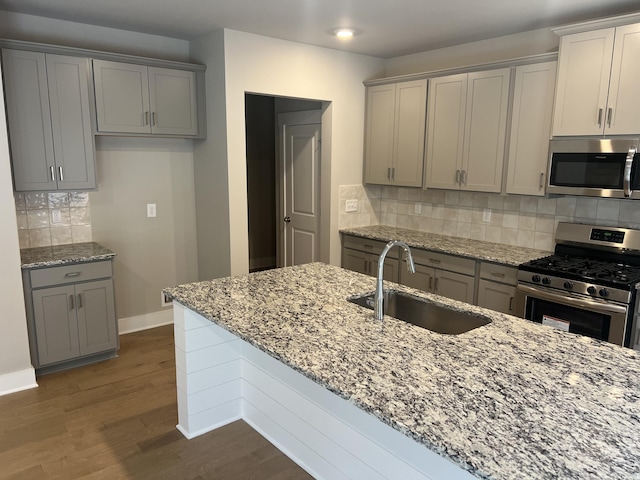 kitchen with light stone countertops, appliances with stainless steel finishes, decorative backsplash, sink, and dark hardwood / wood-style floors