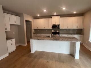 kitchen with a kitchen island with sink, range, white cabinets, sink, and wood-type flooring