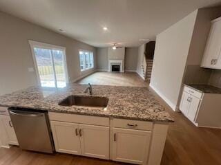 kitchen featuring stainless steel dishwasher, light stone counters, white cabinetry, and sink