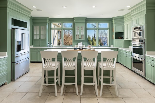 kitchen featuring light tile patterned floors, a kitchen island, green cabinetry, stainless steel appliances, and light countertops