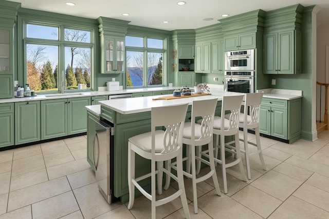 kitchen with a sink, stainless steel double oven, light countertops, green cabinetry, and light tile patterned floors