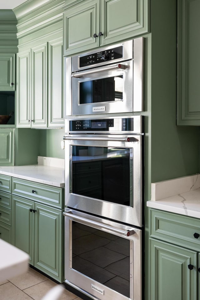 kitchen with green cabinetry, double oven, and light tile patterned floors