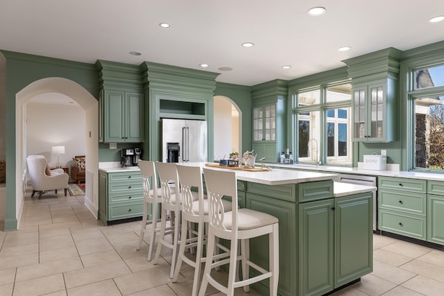 kitchen with a center island, light countertops, high end refrigerator, arched walkways, and green cabinetry