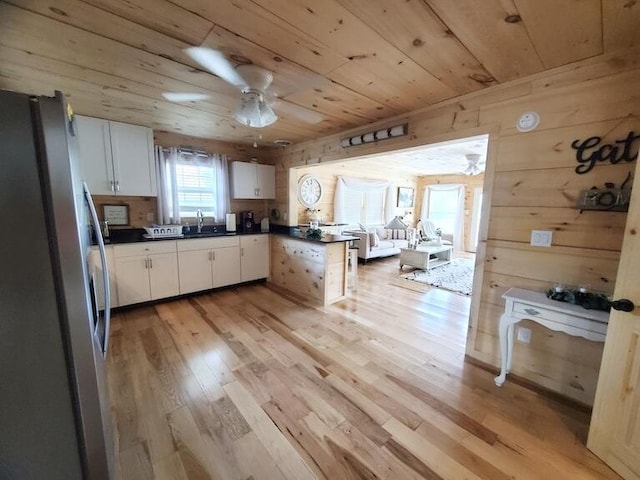 kitchen with stainless steel refrigerator, white cabinetry, light hardwood / wood-style flooring, wood walls, and wood ceiling