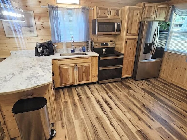 kitchen featuring sink, light stone counters, wood walls, appliances with stainless steel finishes, and light wood-type flooring