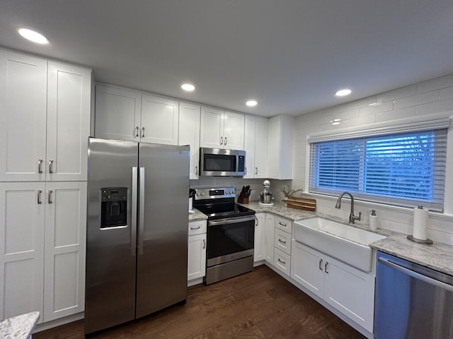 kitchen featuring sink, dark wood-type flooring, light stone counters, white cabinets, and appliances with stainless steel finishes