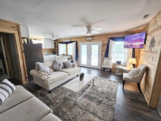 living room featuring ceiling fan, a healthy amount of sunlight, wooden walls, and french doors