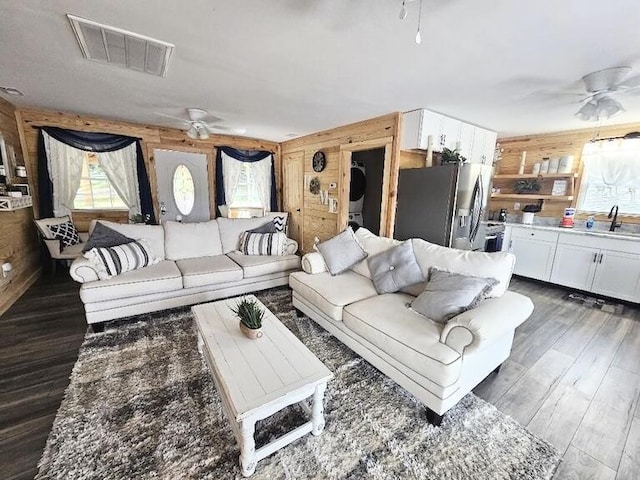 living room featuring dark hardwood / wood-style floors, wood walls, sink, and ceiling fan