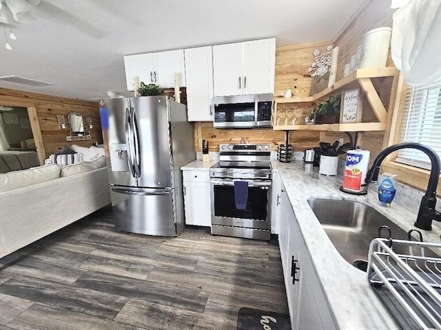 kitchen featuring sink, wooden walls, dark hardwood / wood-style flooring, white cabinetry, and stainless steel appliances