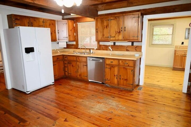 kitchen with white refrigerator with ice dispenser, dishwasher, sink, light wood-type flooring, and beamed ceiling